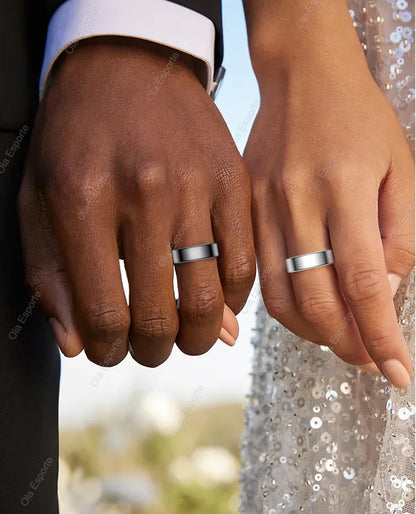 Two hands, one with a dark skin tone and the other with a light skin tone, wearing silver wedding bands against a blurred outdoor background.