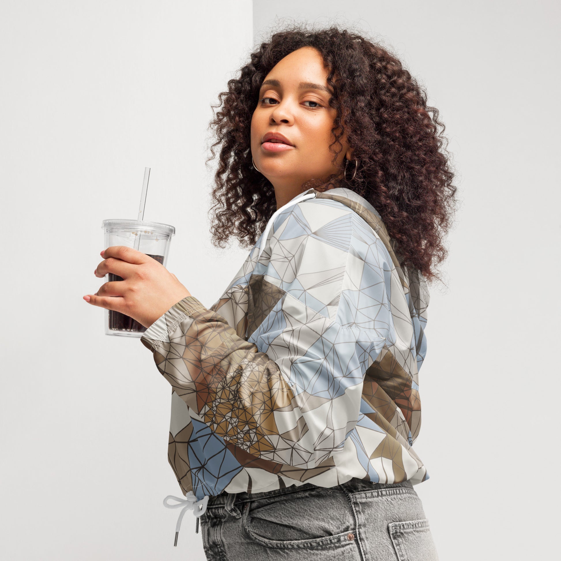 Woman holding a drink with a straw, wearing a patterned jacket against a plain background