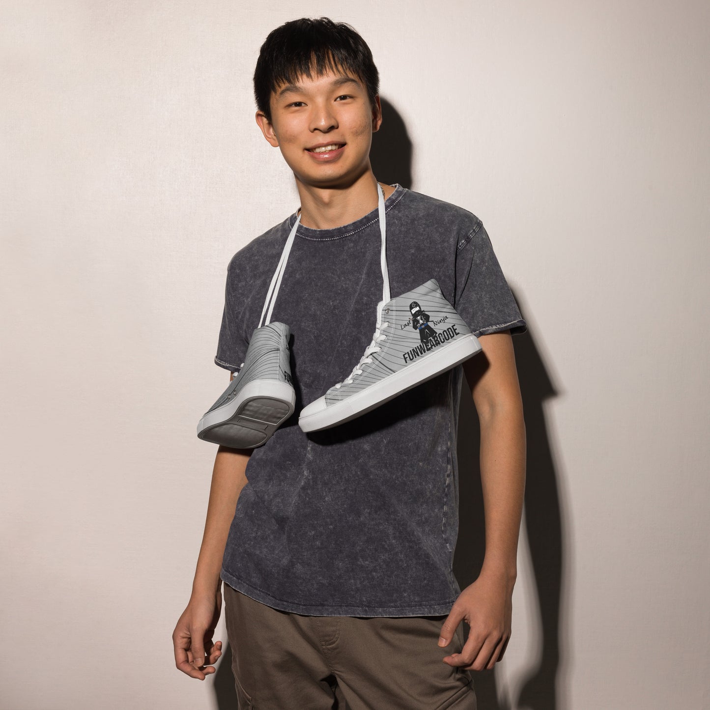 Person holding two sneakers with a ninja graphic and 'Fun Wear Code' text logo against a plain background